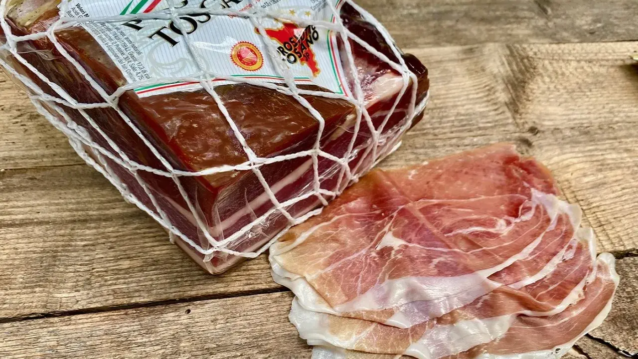 Ein Block **Prosciutto Toscano** im Netz und daneben dünn geschnittene Scheiben.