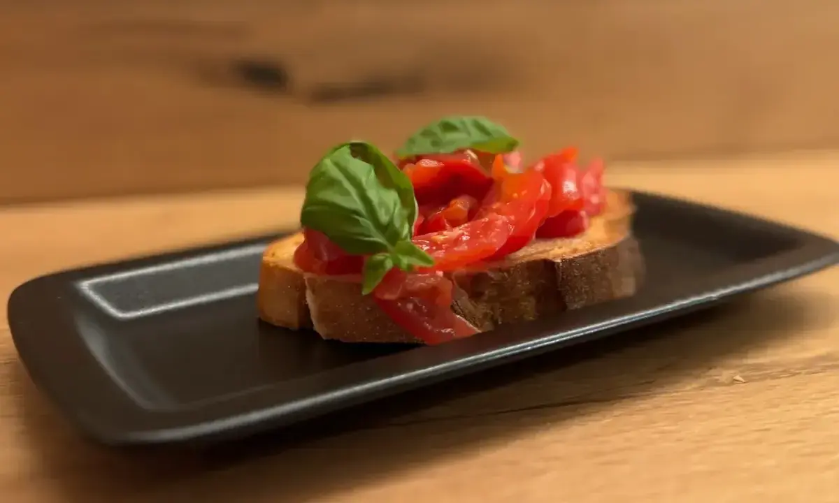 Eine Scheibe geröstetes Brot mit frischen Tomaten und Basilikum, die Haupt-Bruschetta-Zutaten, auf einem schwarzen Teller.