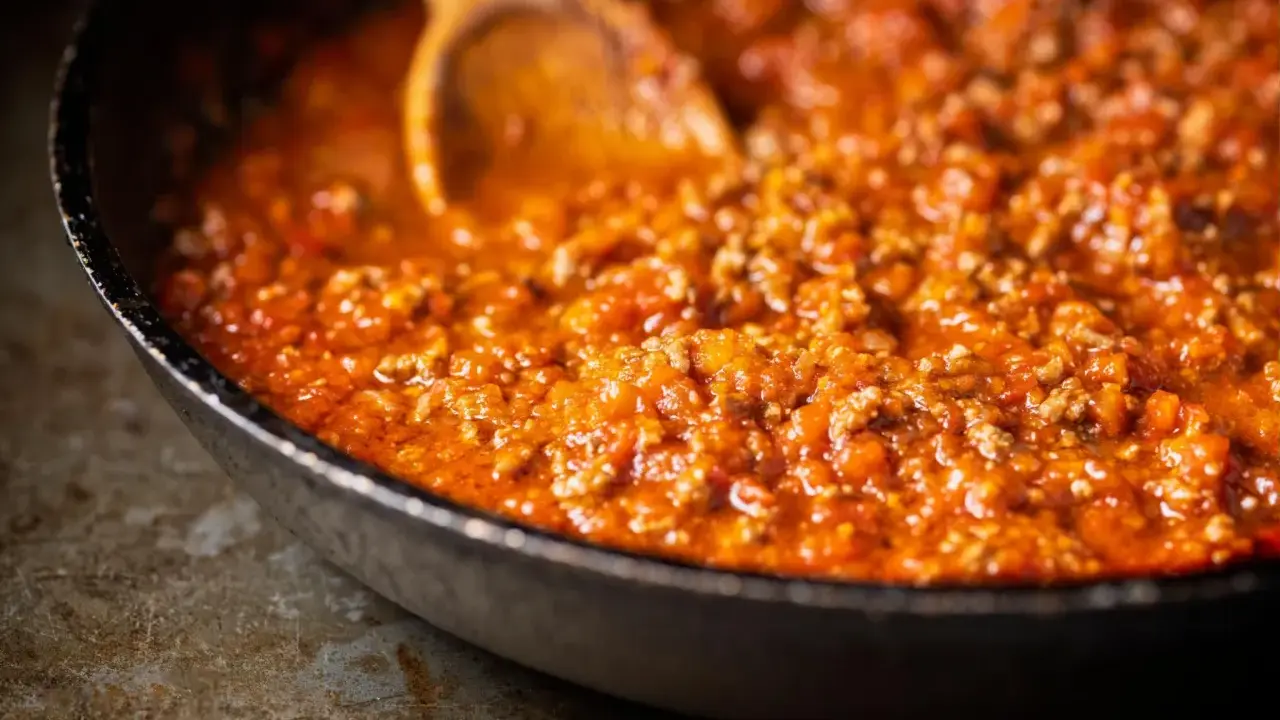 Eine Pfanne mit köstlicher, original italienischer Bolognese-Sauce, die mit einem Holzlöffel umgerührt wird.