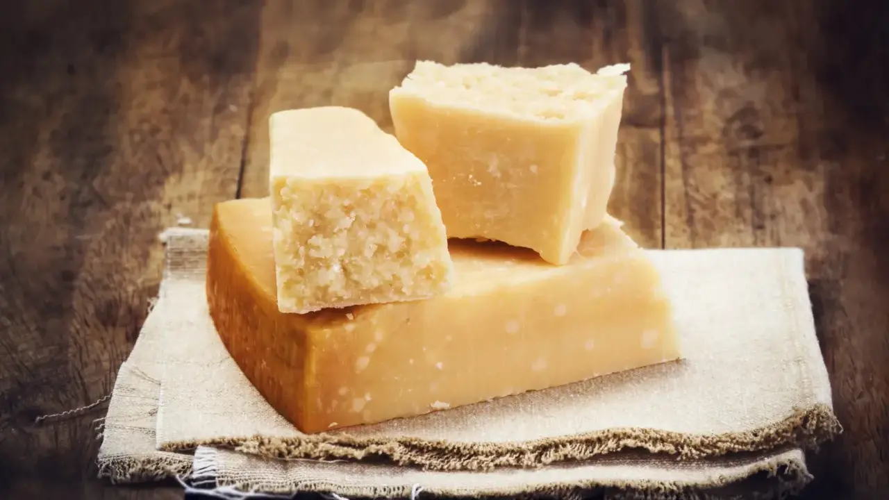 Drei Stücke Hartkäse, vielleicht Pecorino oder Parmesan, liegen auf einem Leinentuch vor rustikalem Holz.