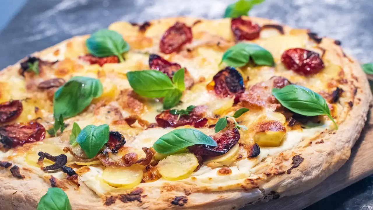 Pizza mit Sahne statt Tomatensauce, belegt mit Kartoffeln, getrockneten Tomaten und frischem Basilikum.