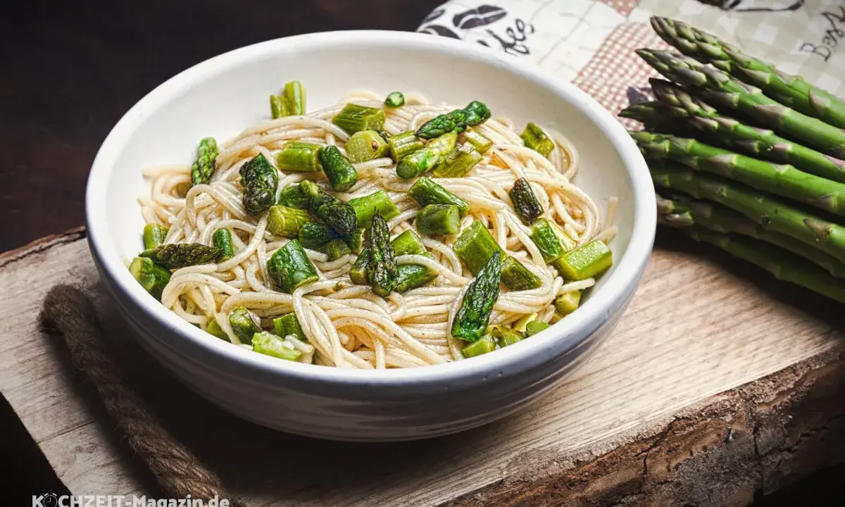 Eine Schüssel mit Spaghetti und frischem Spargel, dane liegt ein Bund grüner Spargel. Ein köstliches Gericht, das Lust auf mehr macht.