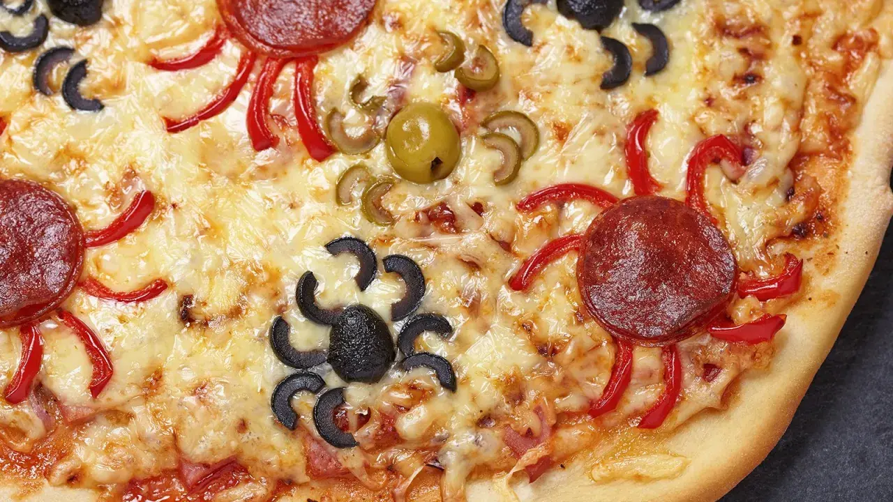 Gruselige Halloween-Pizza mit Spinnen aus Oliven und Salami, die über geschmolzenen Käse krabbeln.