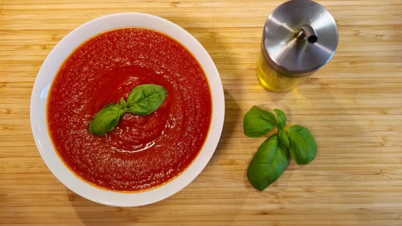 Schüssel mit cremiger Tomatensauce, garniert mit Basilikum. Daneben ein Glas Olivenöl und frische Basilikumblätter. Perfekt für Pasta mit San Marzano Tomaten.