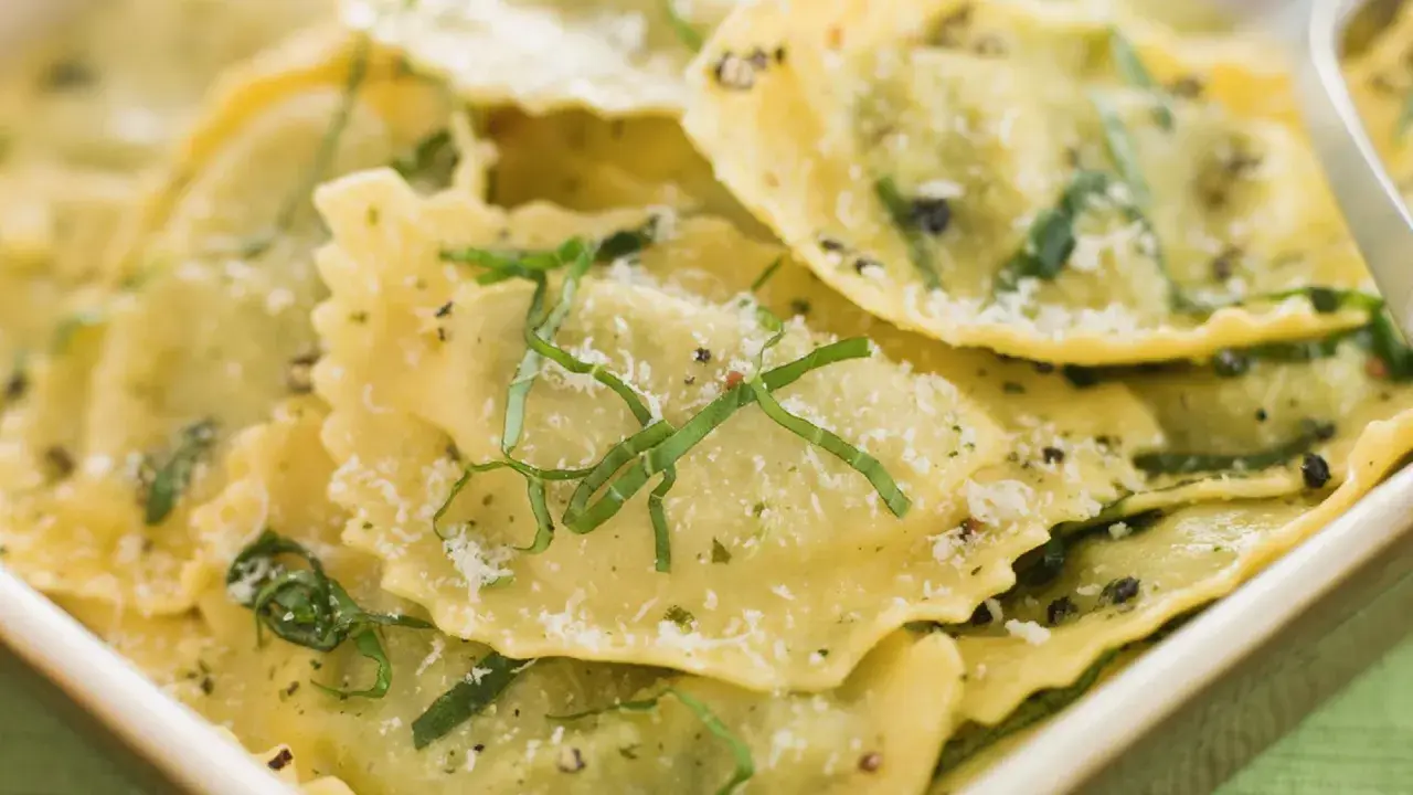 Mezzaluna pasta, gefüllt und mit Kräutern und Parmesan bestreut, liegt appetitlich in einer Schale.