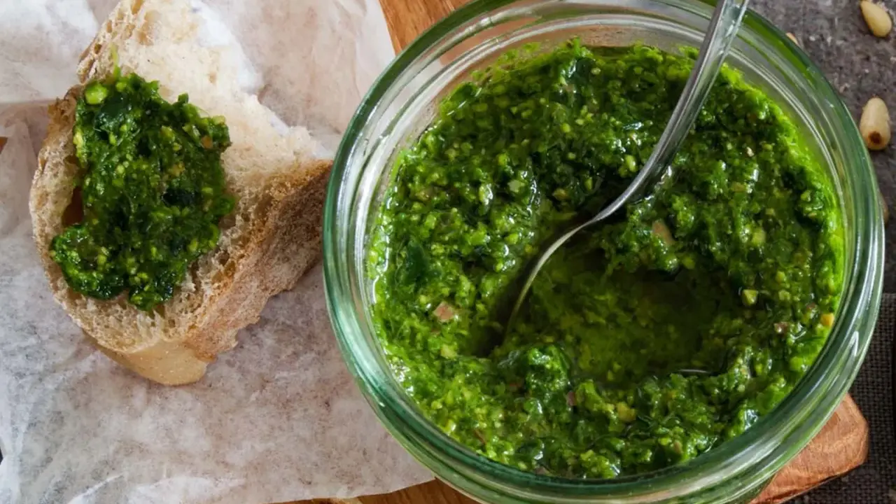 Frisches schnittlauch pesto in einem Glas, mit einem Löffel darin. Ein Stück Brot mit dem grünen Pesto darauf liegt daneben.