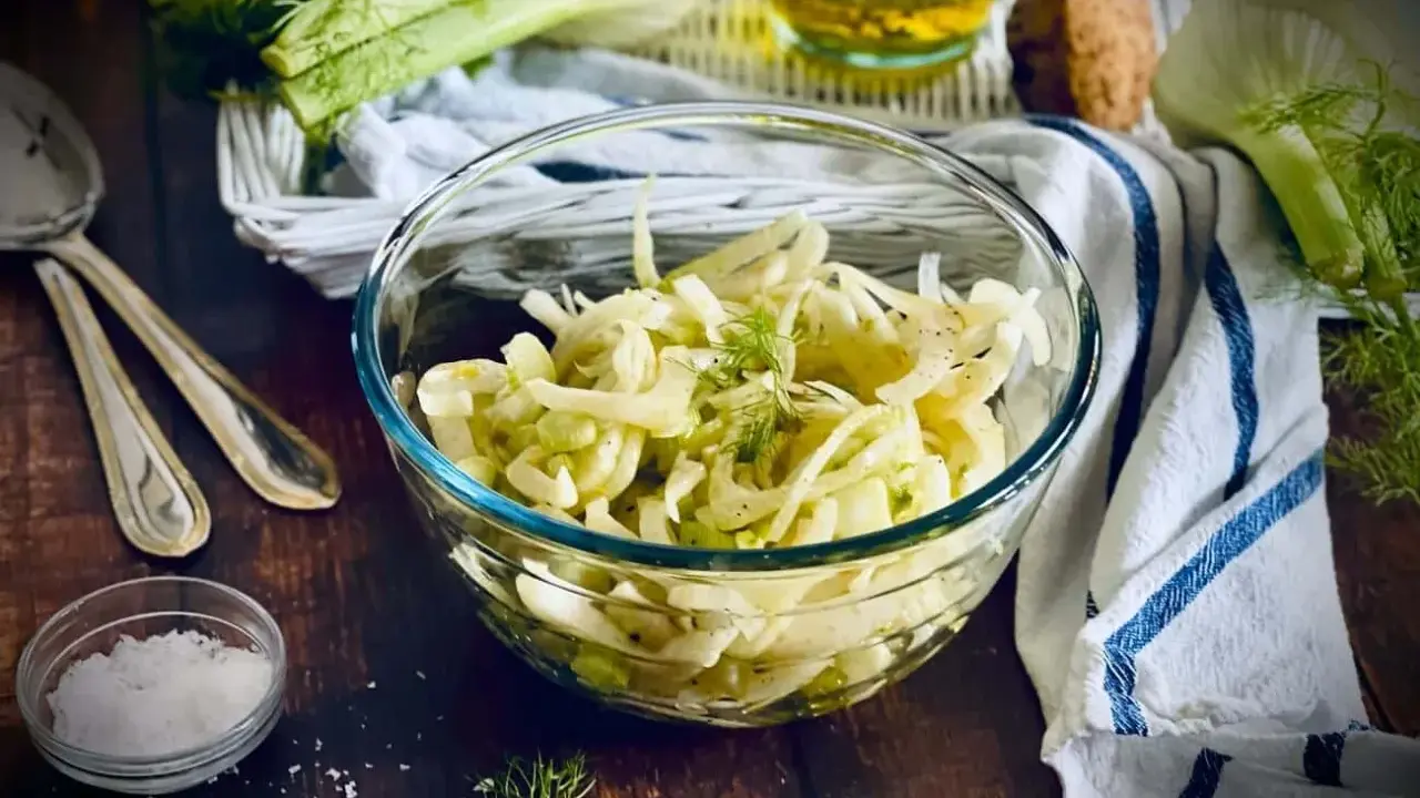 Frischer Fenchel Salat in einer Glasschüssel, garniert mit Dill. Daneben liegen Löffel und eine kleine Schale mit Salz.