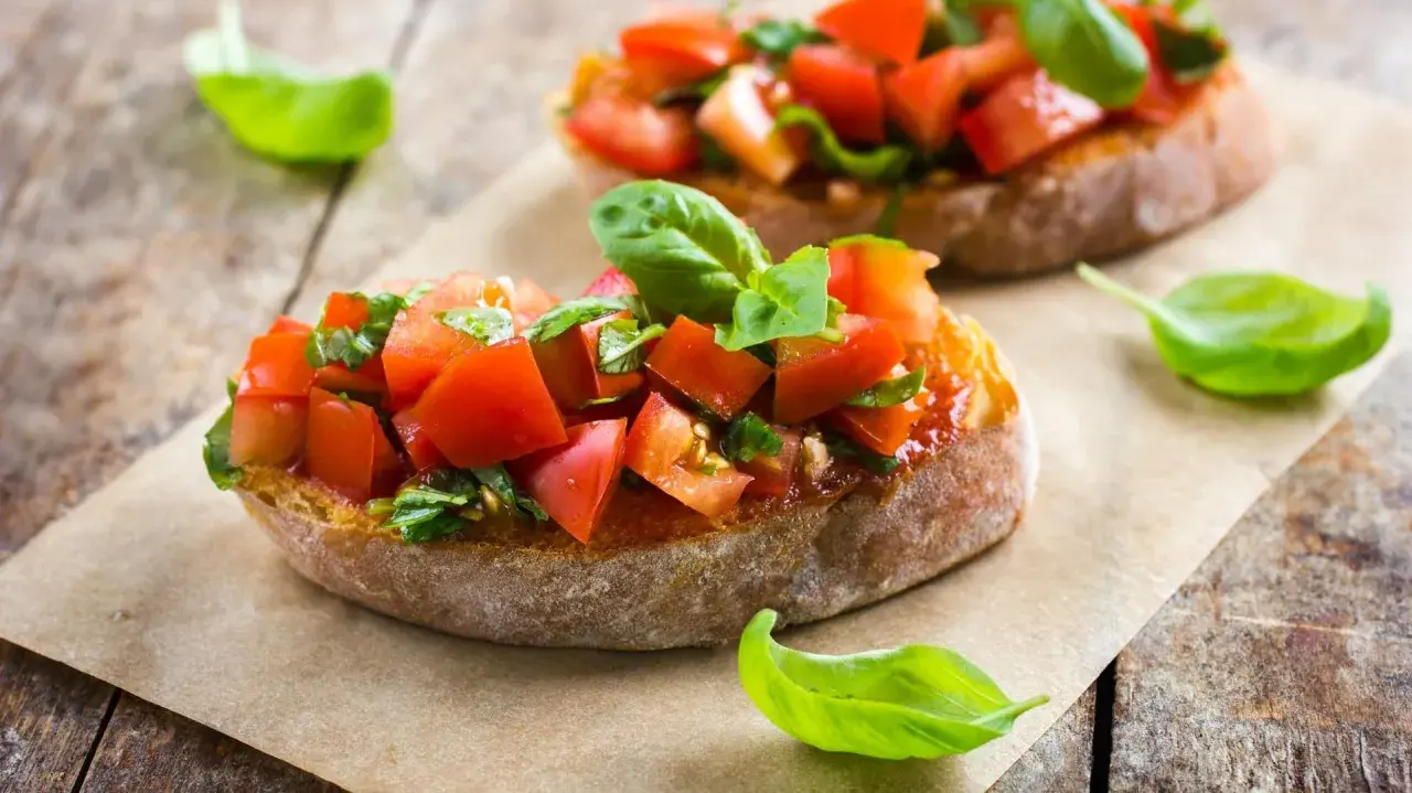 Zwei Bruschetta mit frischen Tomaten und Basilikum, warm oder kalt serviert, auf rustikalem Holztisch.