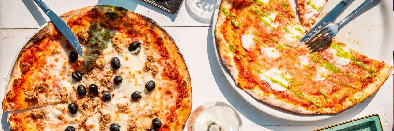 Zwei Pizzen, eine mit Thunfisch und Oliven, die andere mit Pesto. Das Geheimnis einer perfekten Pizza liegt oft im Mehl Typ 00.