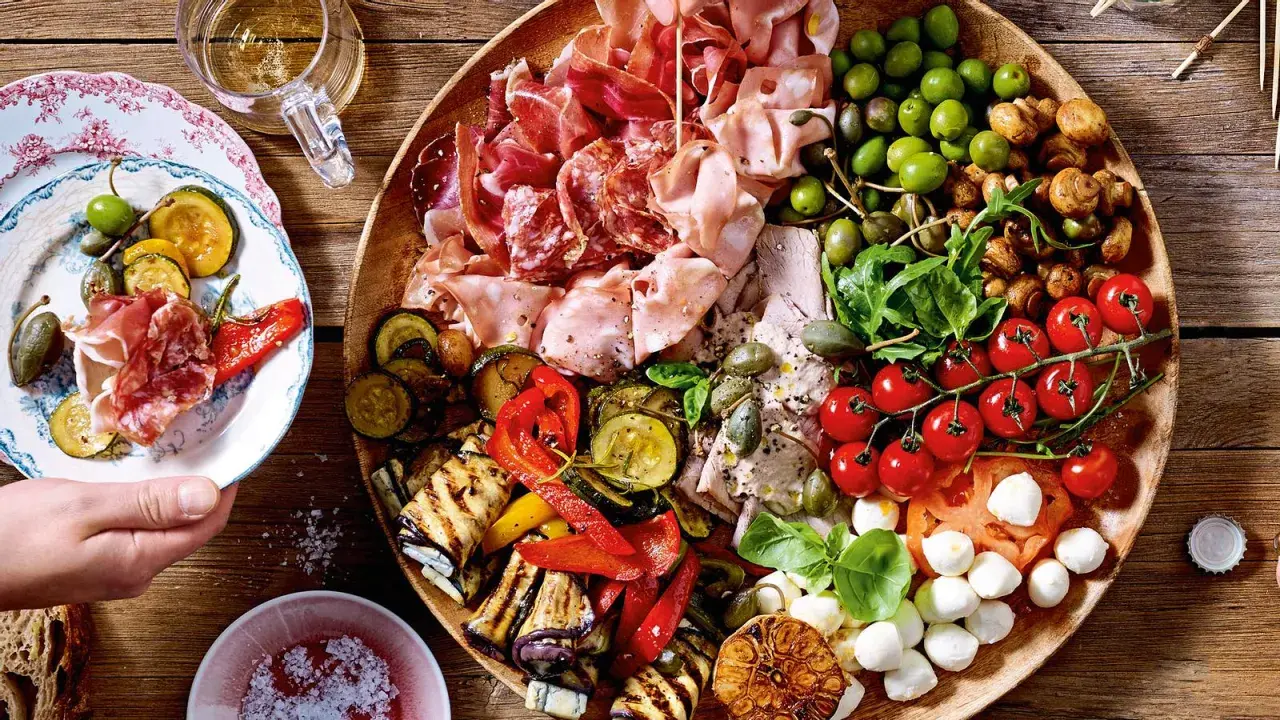 Eine üppige italienische Antipasti-Platte wird liebevoll dekoriert: Wurst, Käse, Oliven, gegrilltes Gemüse und frische Kräuter laden zum Genuss ein.