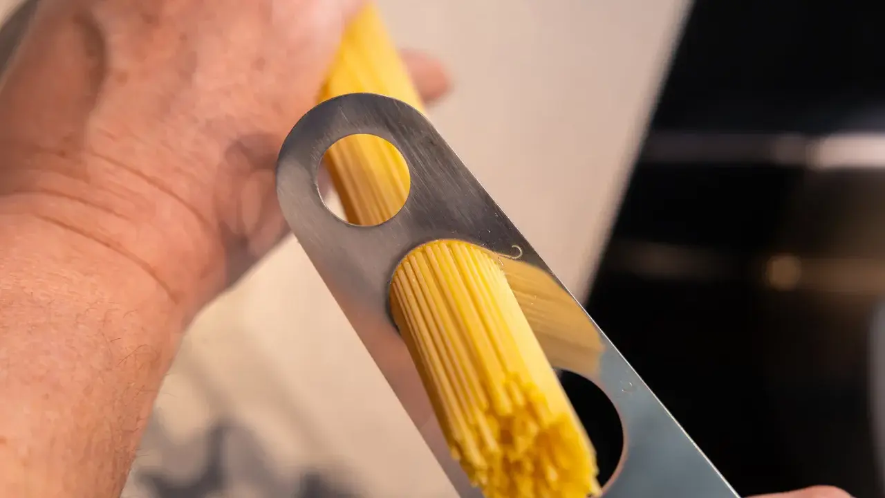 Ein Mann misst mit einem Metallwerkzeug die richtige Menge Spaghetti pro Person ab.