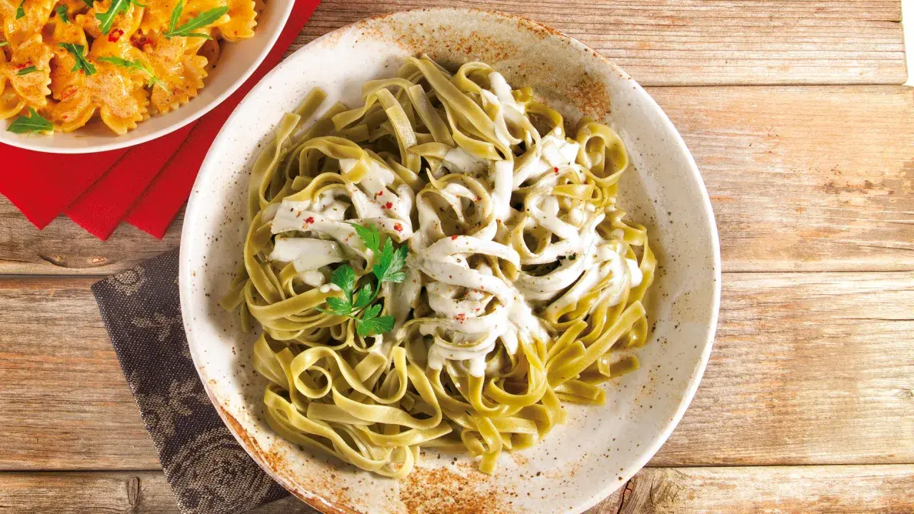 Grüne Bandnudeln mit cremiger Gorgonzola-Sauce, garniert mit Petersilie und roten Pfefferflocken.