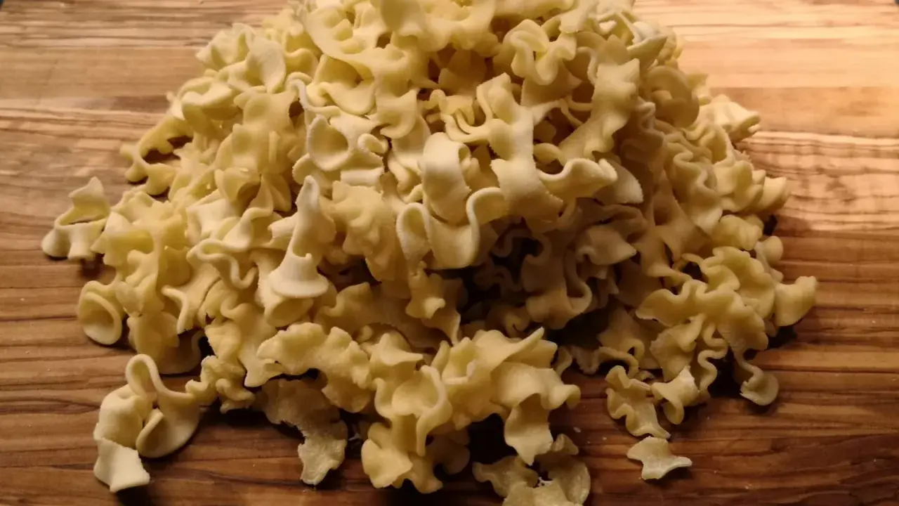 Ein Haufen ungekochte Pasta aus Hartweizengrieß (semola) liegt auf einem Holzbrett.