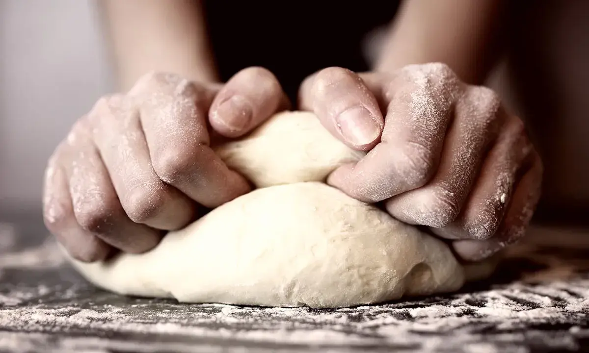 Hände kneten Teig, um die perfekte Konsistenz für Pizza zu erreichen. Die Frage "wie lange pizzateig kneten" beschäftigt viele Hobbybäcker.