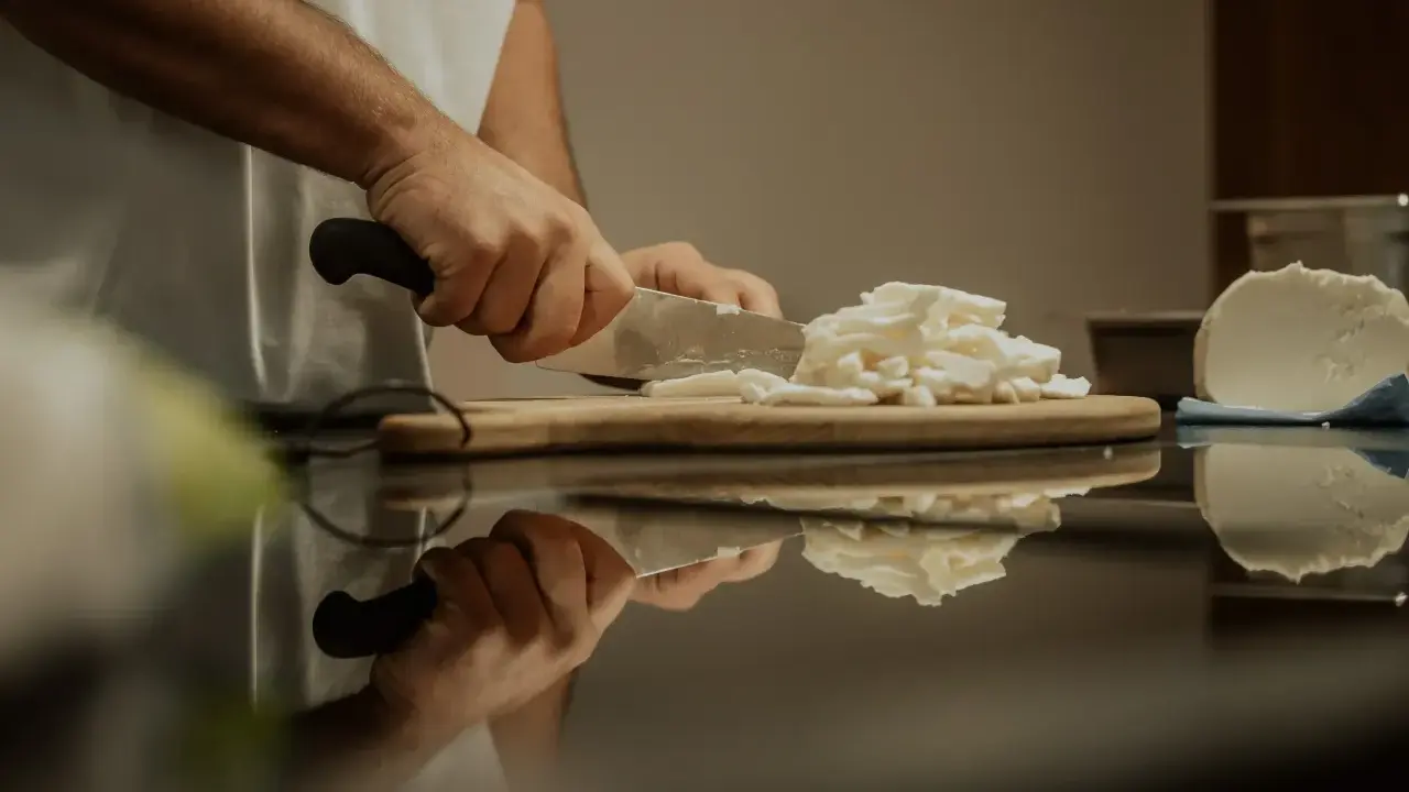 Hände schneiden Fior di Latte auf einem Holzbrett. Die frische Mozzarella-Masse wird für das Einfrieren vorbereitet.