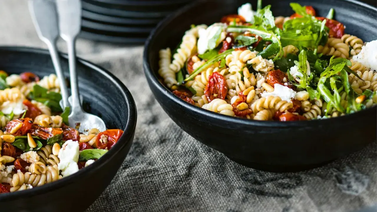 Zwei Schalen mit einem köstlichen nudelsalat mit getrockneten tomaten, Pinienkernen und Rucola.