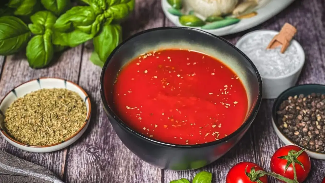 Schüssel mit original italienischer pizzasauce, umgeben von frischem Basilikum, Tomaten, Knoblauch, Salz und Pfeffer.