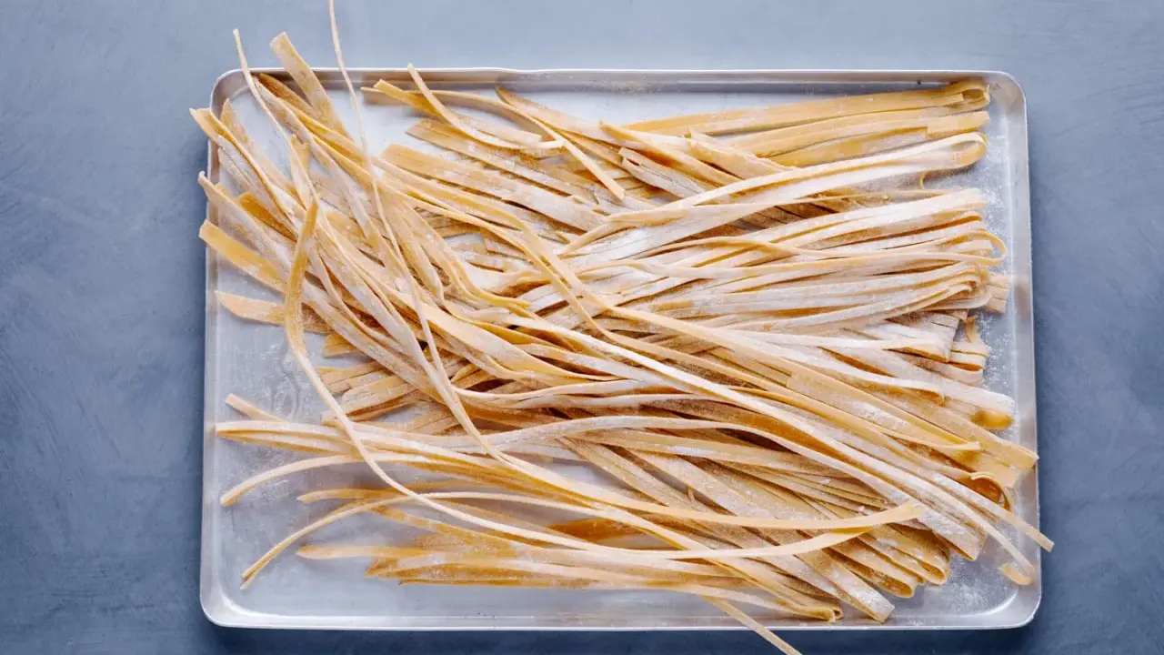Frische, selbstgemachte Tagliatelle liegen auf einem Blech, bereit zum Kochen. Das Ergebnis von Tagliatelle selber machen.