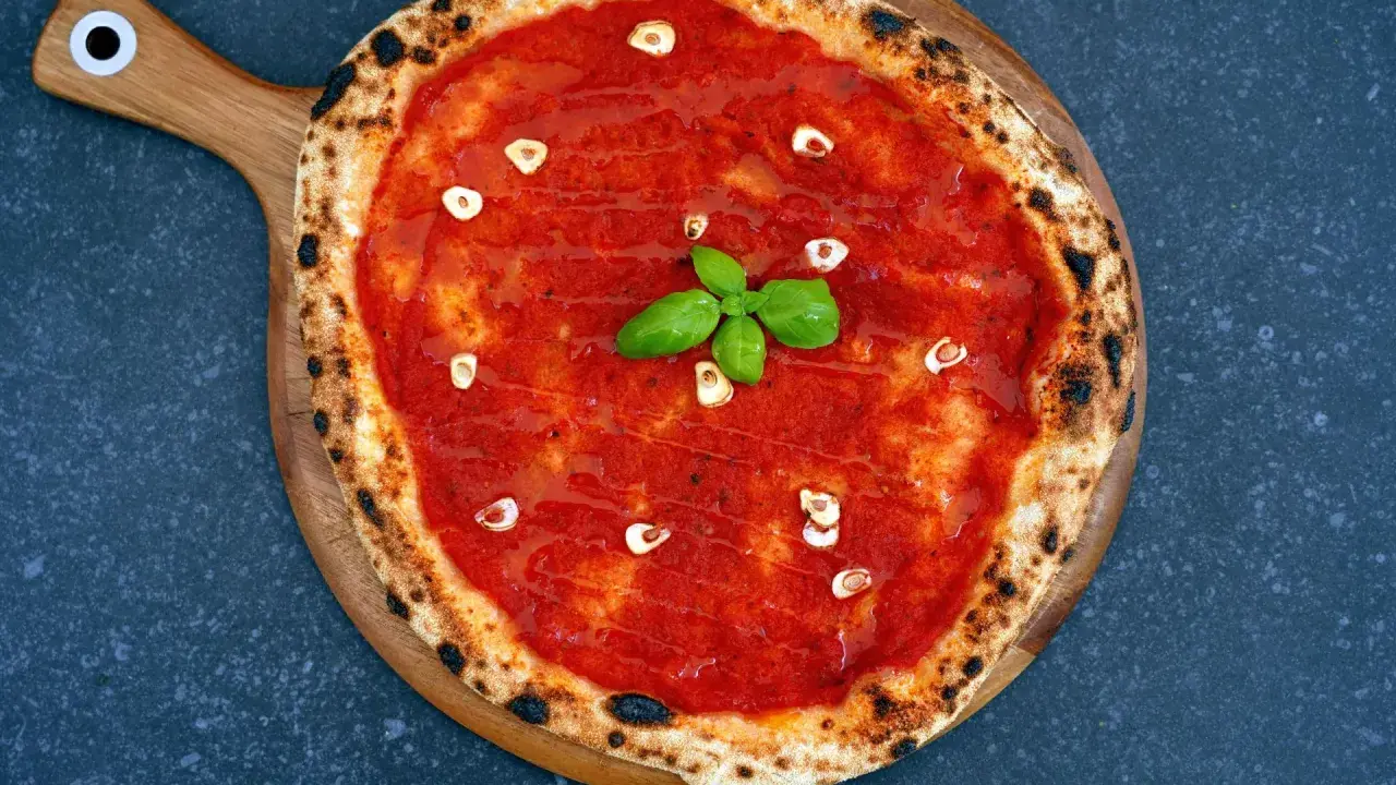 Eine köstliche Pizza Marinara mit Tomatensauce, Knoblauchscheiben und frischem Basilikum auf einem Holzbrett.