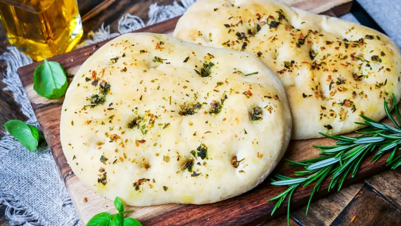 Zwei fluffige Pizzabrote mit Kräutern, perfekt gebacken mit Trockenhefe. Daneben frisches Basilikum und Rosmarin.