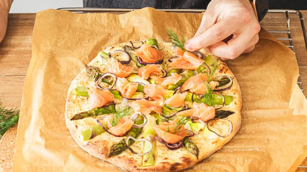 Eine köstliche Pizza mit Lachs, Spargel und roten Zwiebeln wird mit frischem Dill garniert.