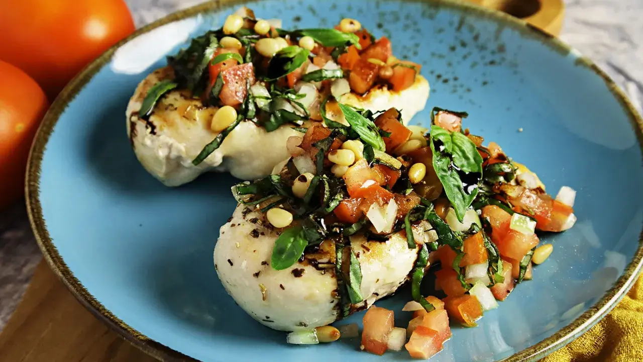 Zwei Hähnchenbrustfilets mit frischer Tomaten-Basilikum-Mischung und Pinienkernen, beträufelt mit Balsamico. Köstliche Bruschetta-Variante.