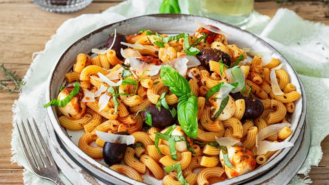 Ein köstlicher mediterraner Nudelsalat mit Pasta, Oliven, Mozzarella-Bällchen und frischem Basilikum, garniert mit Parmesan.
