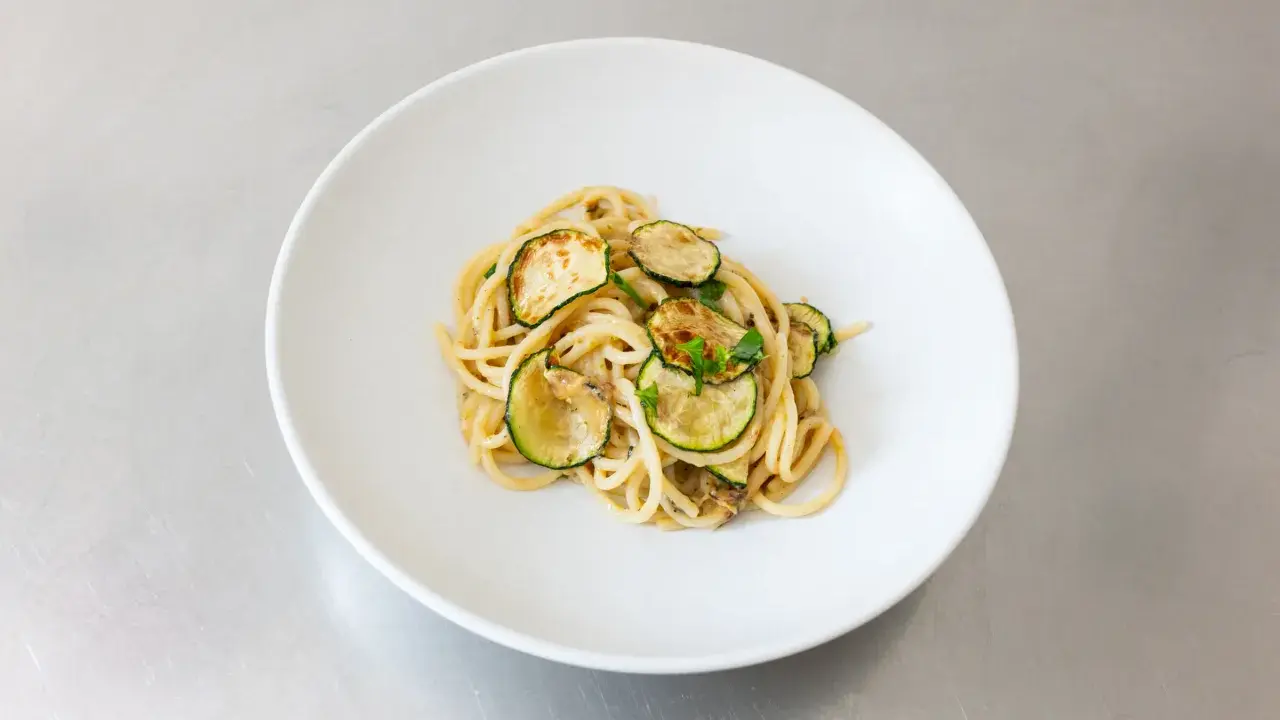 Spaghetti alla Nerano, ein cremiges Pastagericht mit gebratenen Zucchinischeiben, garniert mit frischen Kräutern, serviert auf einem weißen Teller.
