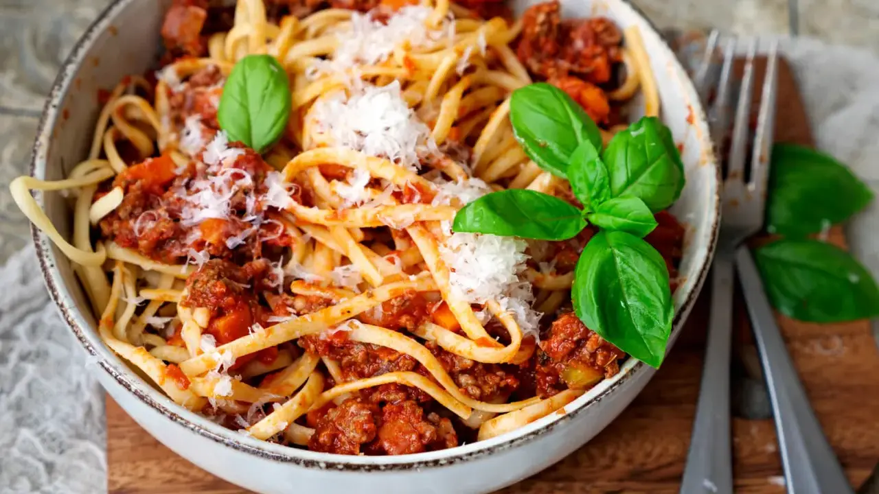 Eine Schüssel mit Linguine und einer herzhaften, **schnellen Bolognese**. Garniert mit frischem Basilikum und Parmesan.
