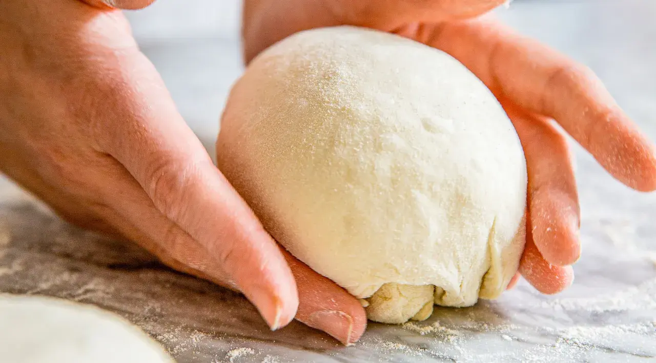 Hände formen einen Teigball, bereit zum stretch and fold pizza.