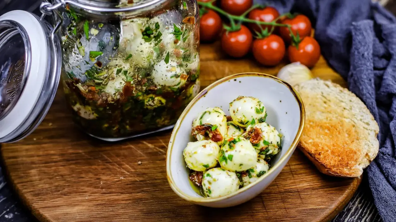 Marinierte Mozzarellakugeln in einem Glas, bereit für köstliche Mozzarella Rezepte. Dazu gibt es frische Tomaten und geröstetes Brot.