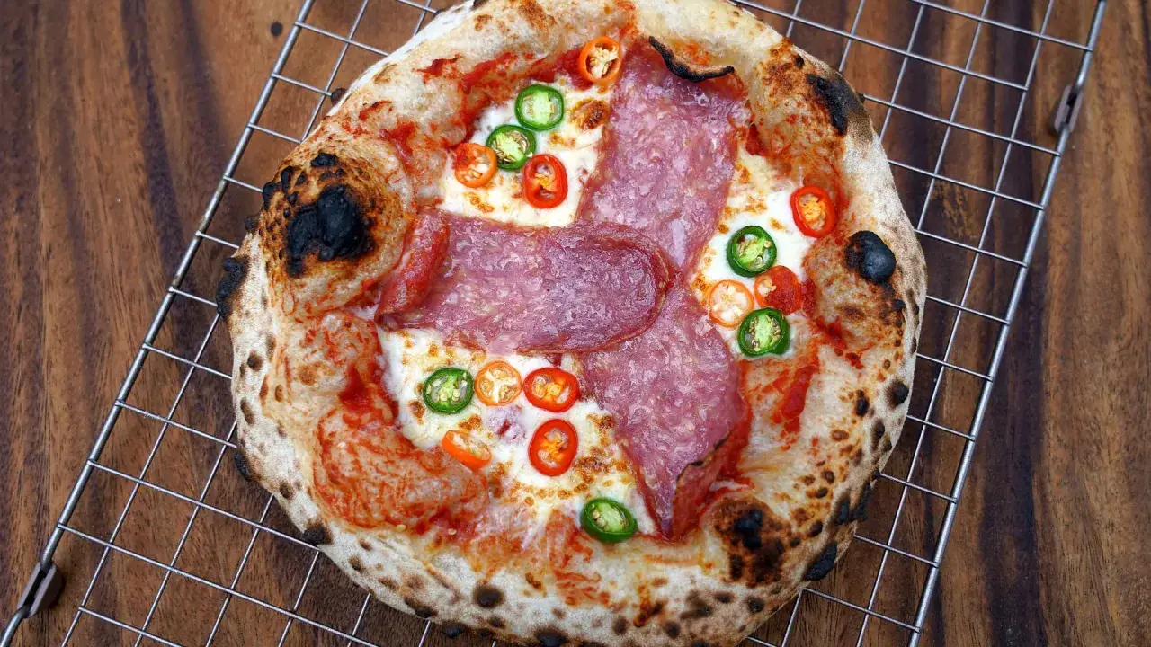 Eine scharfe Salami Pizza mit geschmolzenem Käse und bunten Chilischeiben auf einem Gitterrost.