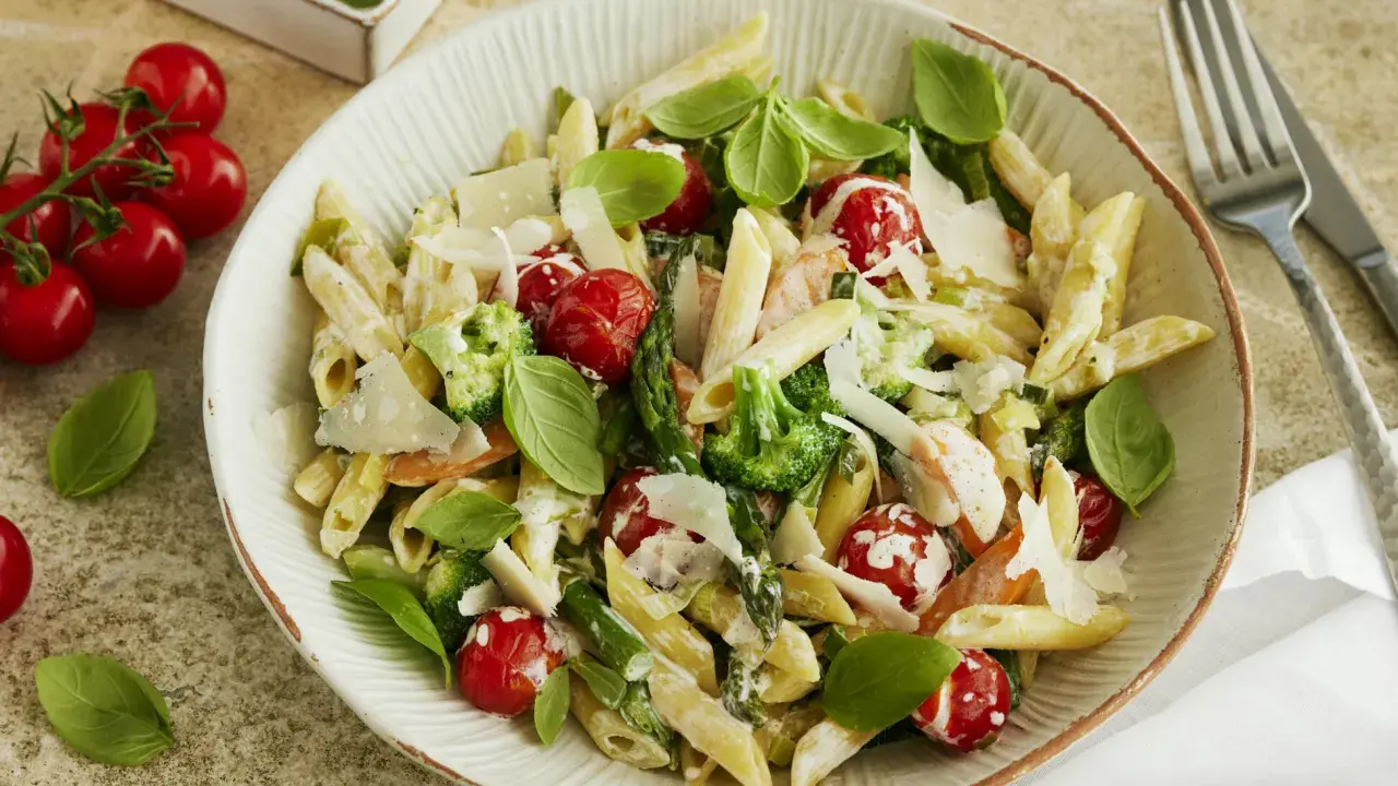 Pasta Primavera mit Penne, Brokkoli, Kirschtomaten, Spargel und Parmesan. Frisches Basilikum garniert dieses köstliche Gericht.