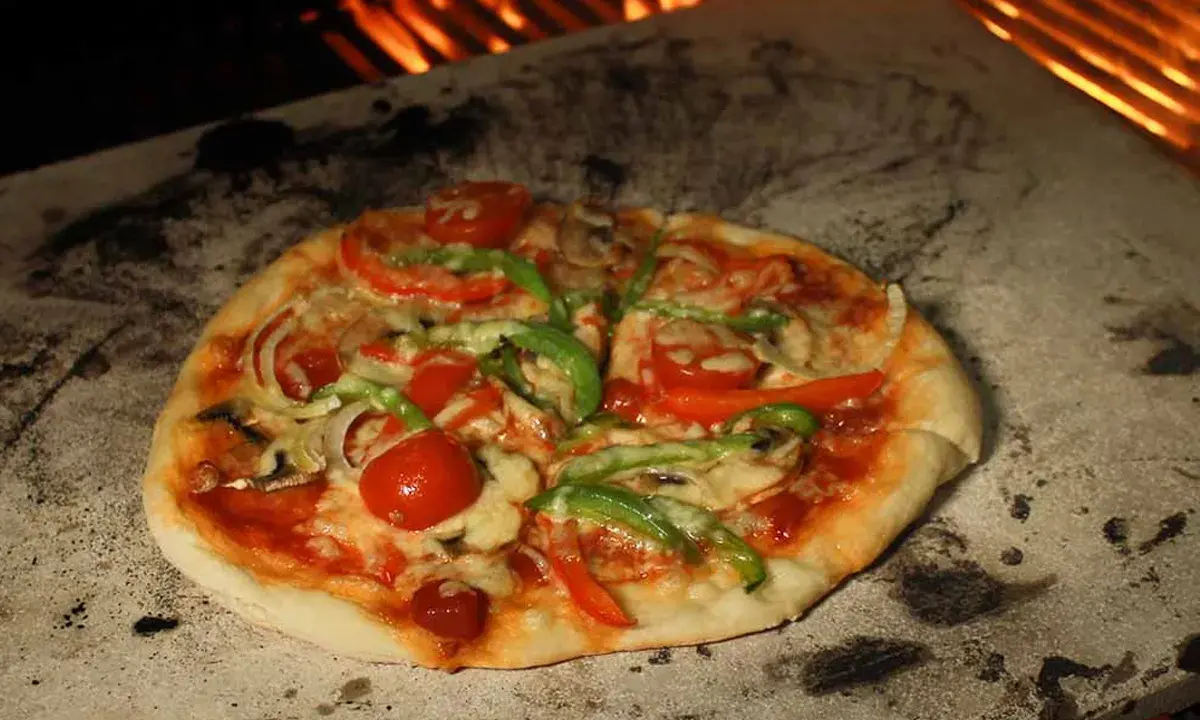 Eine köstliche Pizza mit Tomaten, Paprika und Pilzen wird auf einem Pizzastein im Ofen gebacken, wo die Flammen lodern.