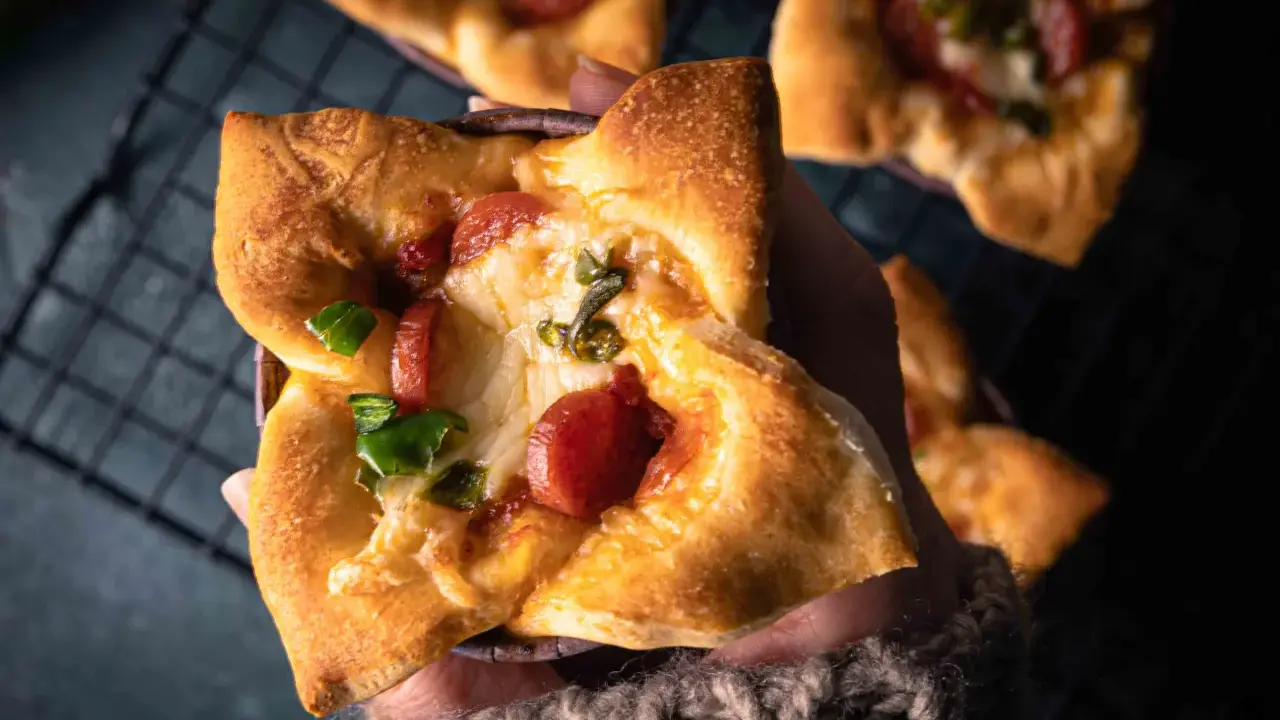 Hand hält einen herzhaften Pizza-Muffin mit geschmolzenem Käse, Wurst und grünen Paprika.