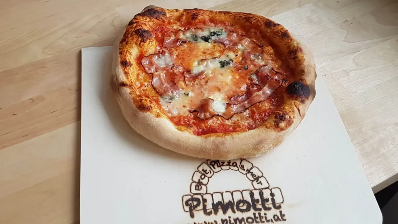 Eine knusprige Pancetta Pizza mit geschmolzenem Käse und Tomatensauce auf einem Holzbrett.