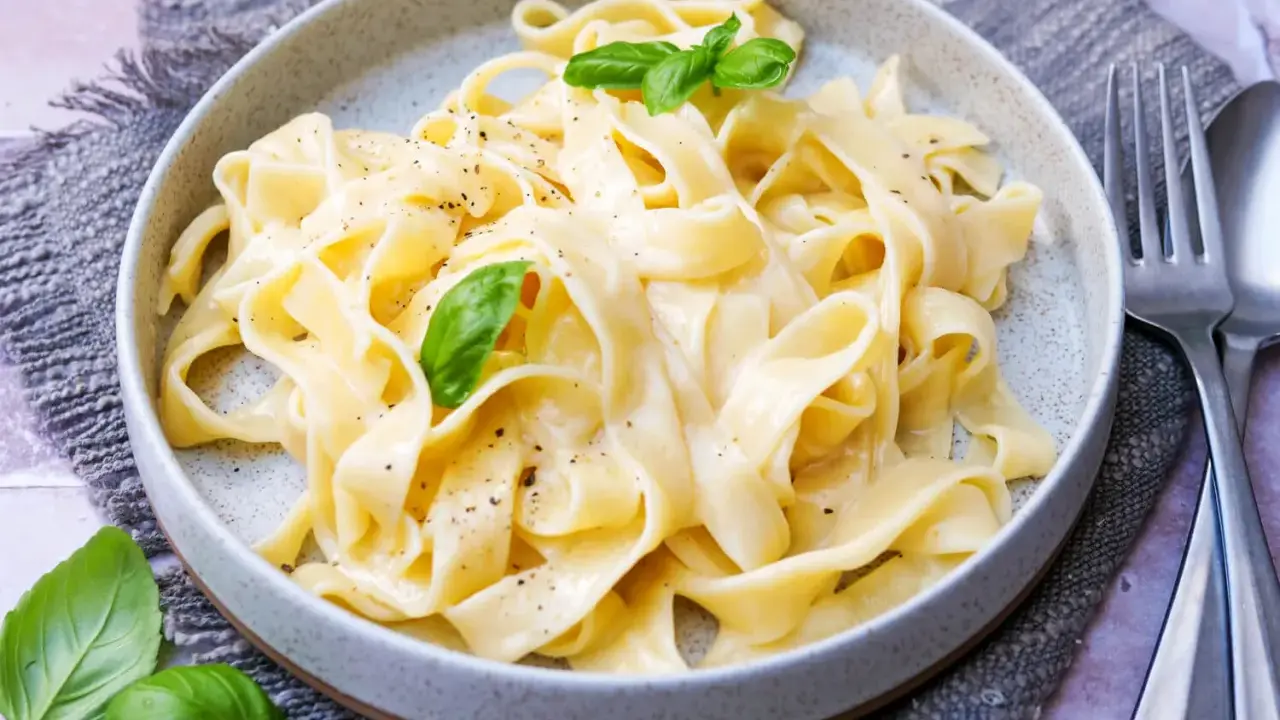 Cremige Pasta Alfredo mit frischem Basilikum und schwarzem Pfeffer, serviert auf einem grauen Tischtuch.