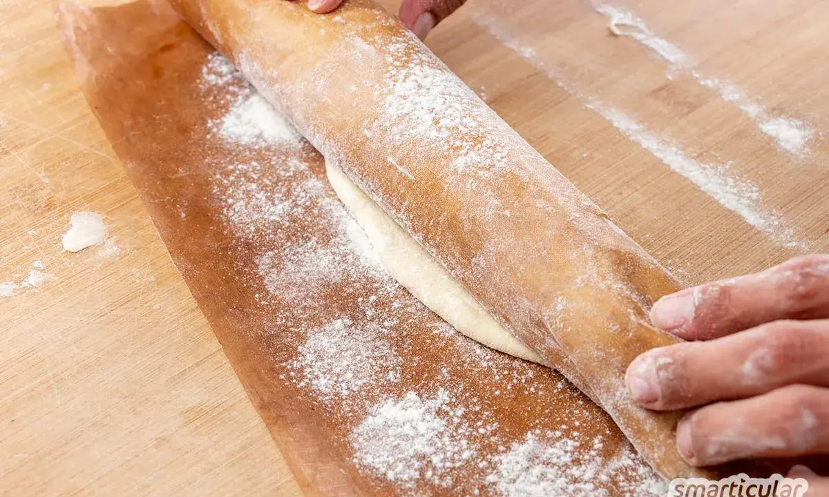 Hände rollen Teig auf Backpapier aus. Perfekt, um gegangenen Pizzateig einzufrieren und später zu verwenden.
