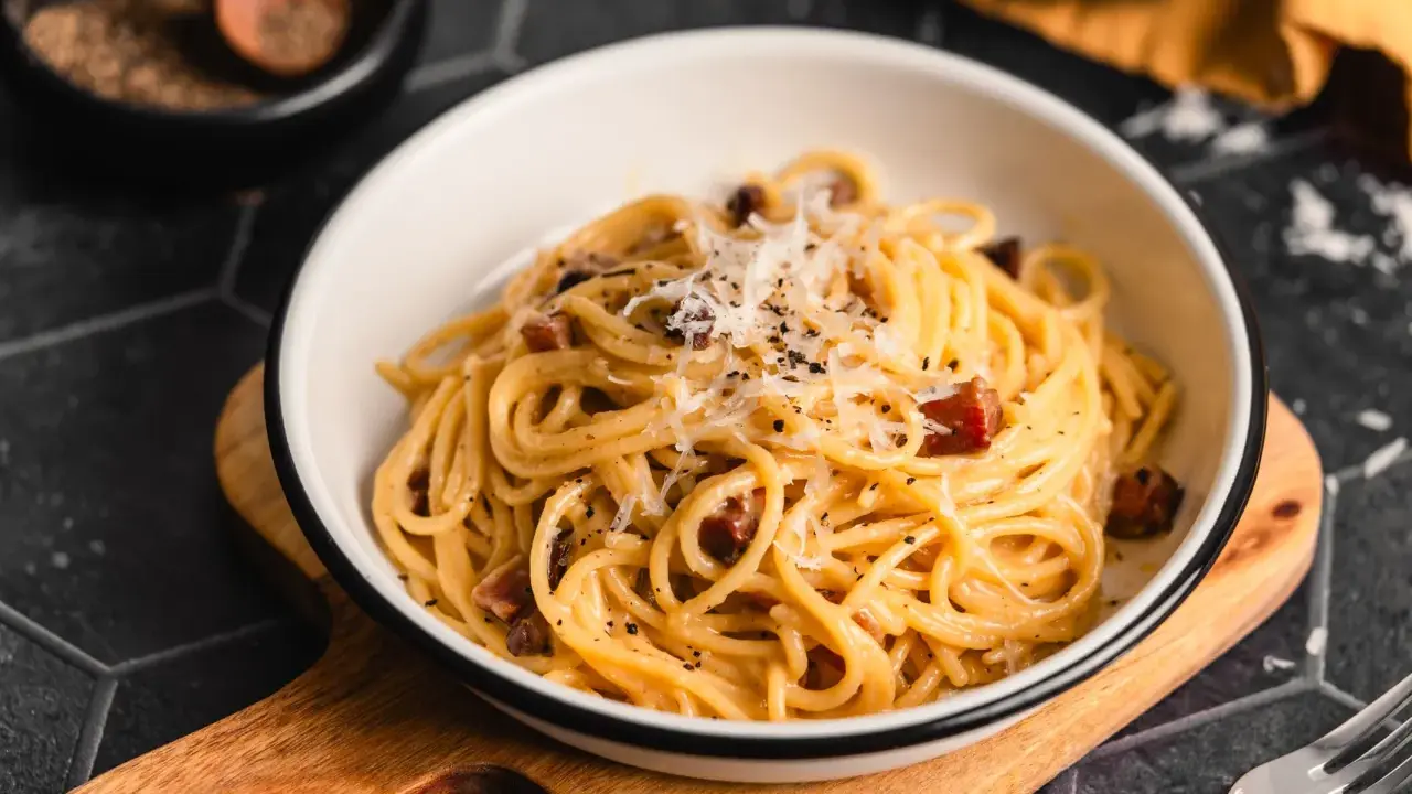 Eine Schüssel cremiger Spaghetti Carbonara, bestreut mit Parmesan und schwarzem Pfeffer, bereit zum Genießen.