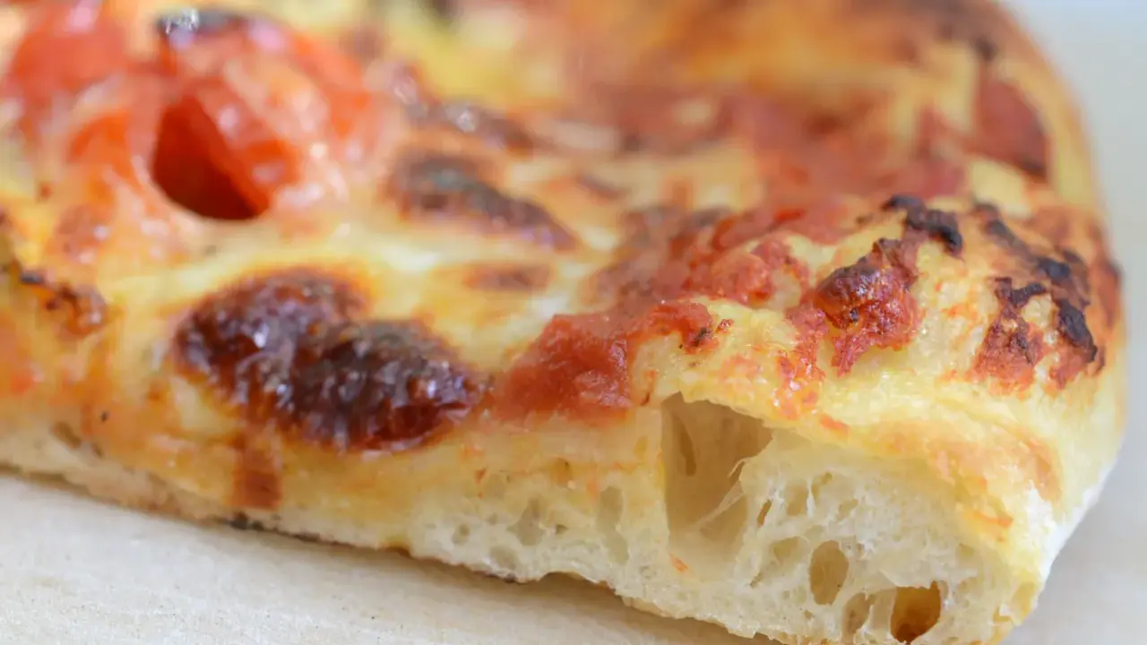 Ein Stück Pizza mit luftigem pizzateig, frisch aus dem pizzaofen. Der Teig ist goldbraun gebacken, die Tomatensoße und der Käse sind perfekt geschmolzen.