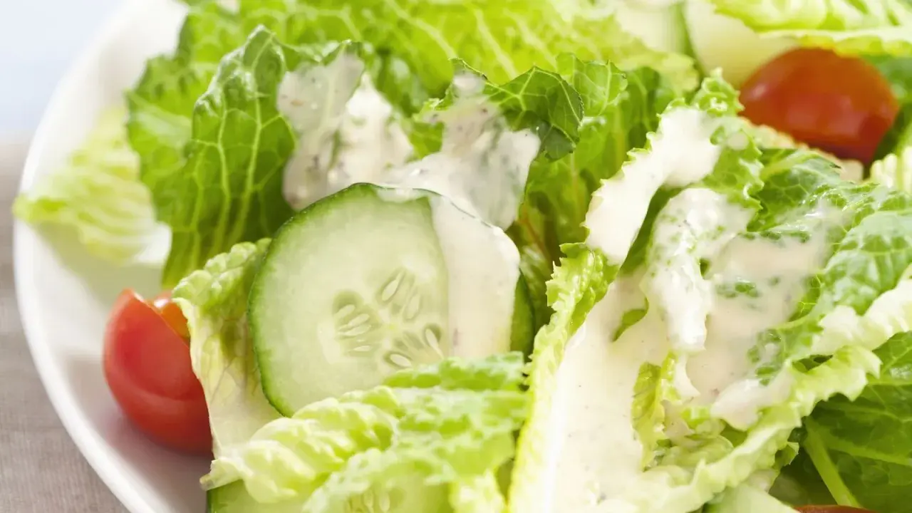 Frischer Romana Salat mit Gurkenscheiben und Tomaten, beträufelt mit cremigem Dressing.