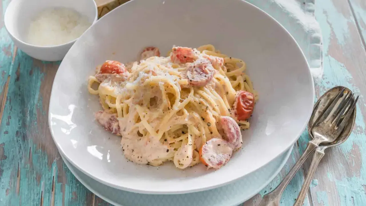 Cremige Pasta al Salmone mit Kirschtomaten und Parmesan, serviert auf einem rustikalen Holztisch.
