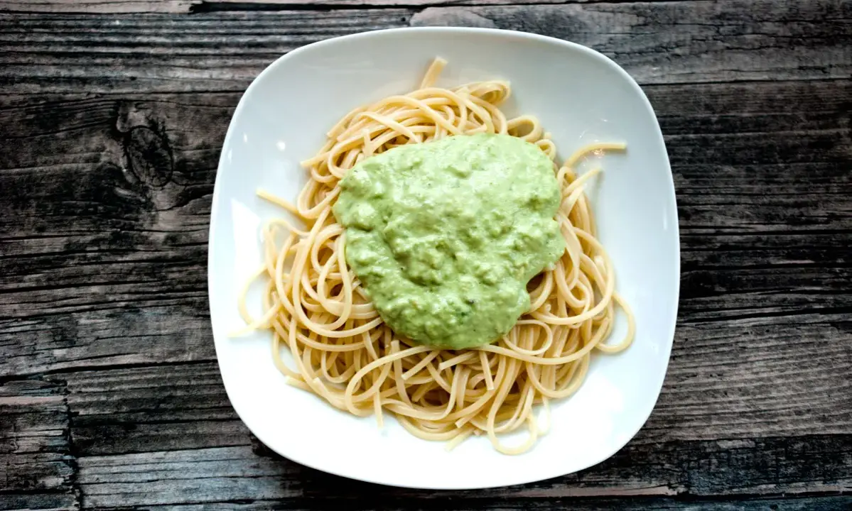 Spaghetti mit cremigem Avocado Pesto auf einem weißen Teller, serviert auf rustikalem Holz.
