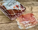Ein Block **Prosciutto Toscano** im Netz und daneben dünn geschnittene Scheiben.