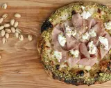 Pizza mit Mortadella, Pistazien und cremigem Käse, daneben einige Pistazien und eine Zitronenspalte.