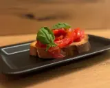 Eine Scheibe geröstetes Brot mit frischen Tomaten und Basilikum, die Haupt-Bruschetta-Zutaten, auf einem schwarzen Teller.