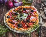 Herzhafte Gyros Pizza mit Zwiebeln, Oliven und Kräutern, serviert auf einem Teller mit Gabel und Messer.