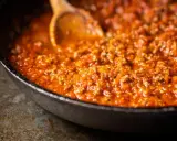 Eine Pfanne mit köstlicher, original italienischer Bolognese-Sauce, die mit einem Holzlöffel umgerührt wird.