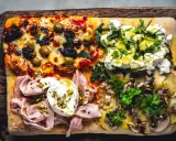 Vier verschiedene Beläge auf einer rechteckigen Pizza in Teglia: Oliven & Tomaten, Ricotta & Kräuter, Mortadella & Burrata, Kartoffeln & Pilze.