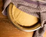 Frischer, aufgegangener Pizzateig ruht in einer Schüssel, bedeckt mit einem gemusterten Tuch. Perfekt für Ihr Pizzateig Rezept.